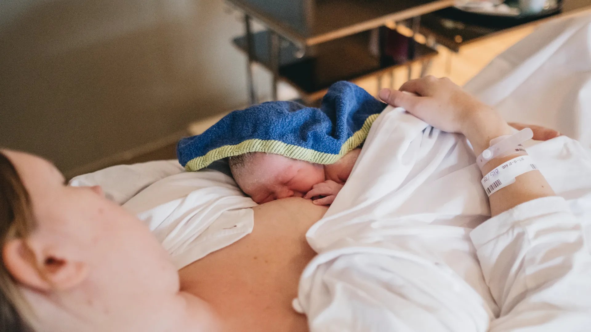 En kvinna som ligger i sängen med en bebis insvept i en filt.